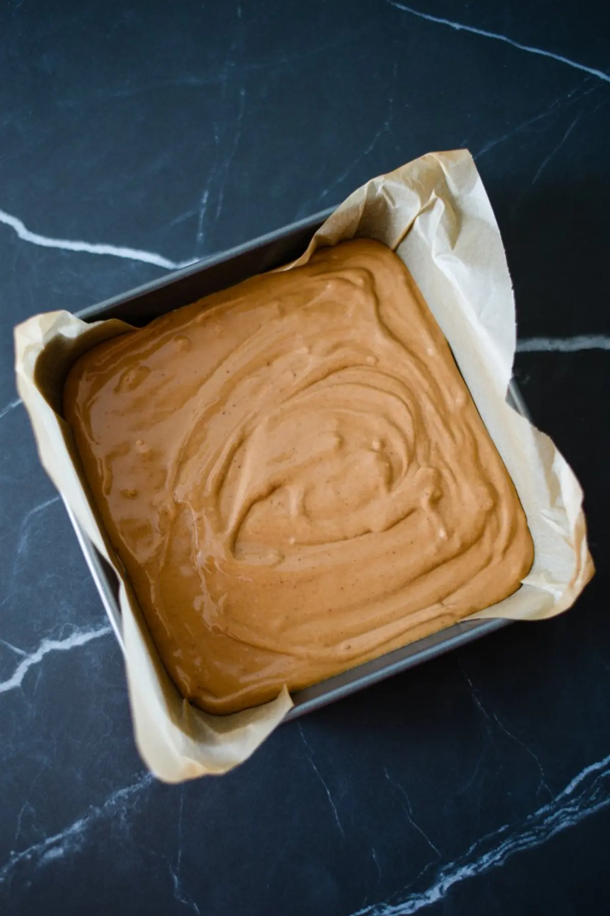 Unbaked gingerbread fudge batter evenly spread in a parchment-lined square baking pan, ready to be set.