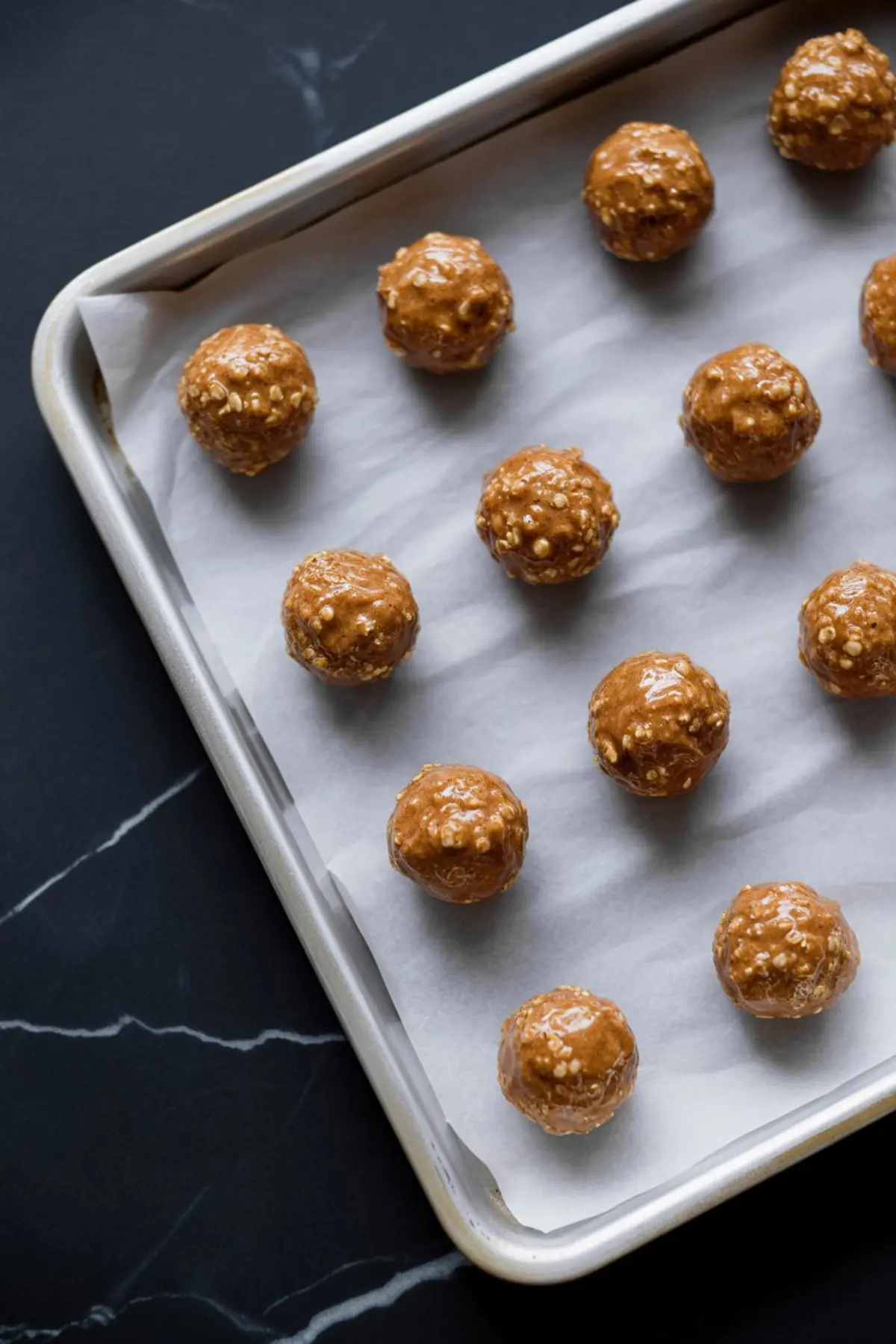 Peanut butter quinoa energy bites evenly spaced on a parchment lined baking sheet, showing glossy peanut butter coating and quinoa pieces before chilling.