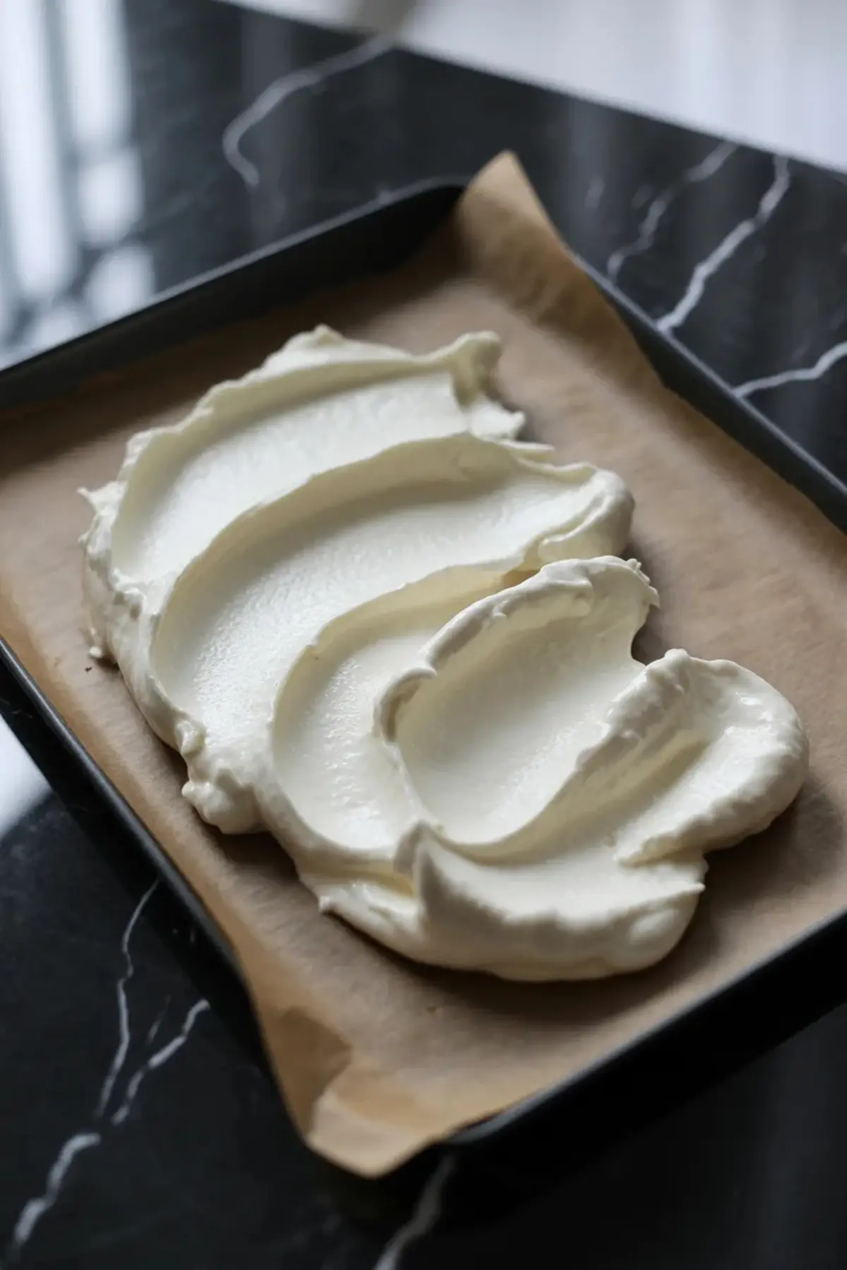 Greek yogurt is spread into an even layer on a parchment-lined tray for peach yogurt bark.
