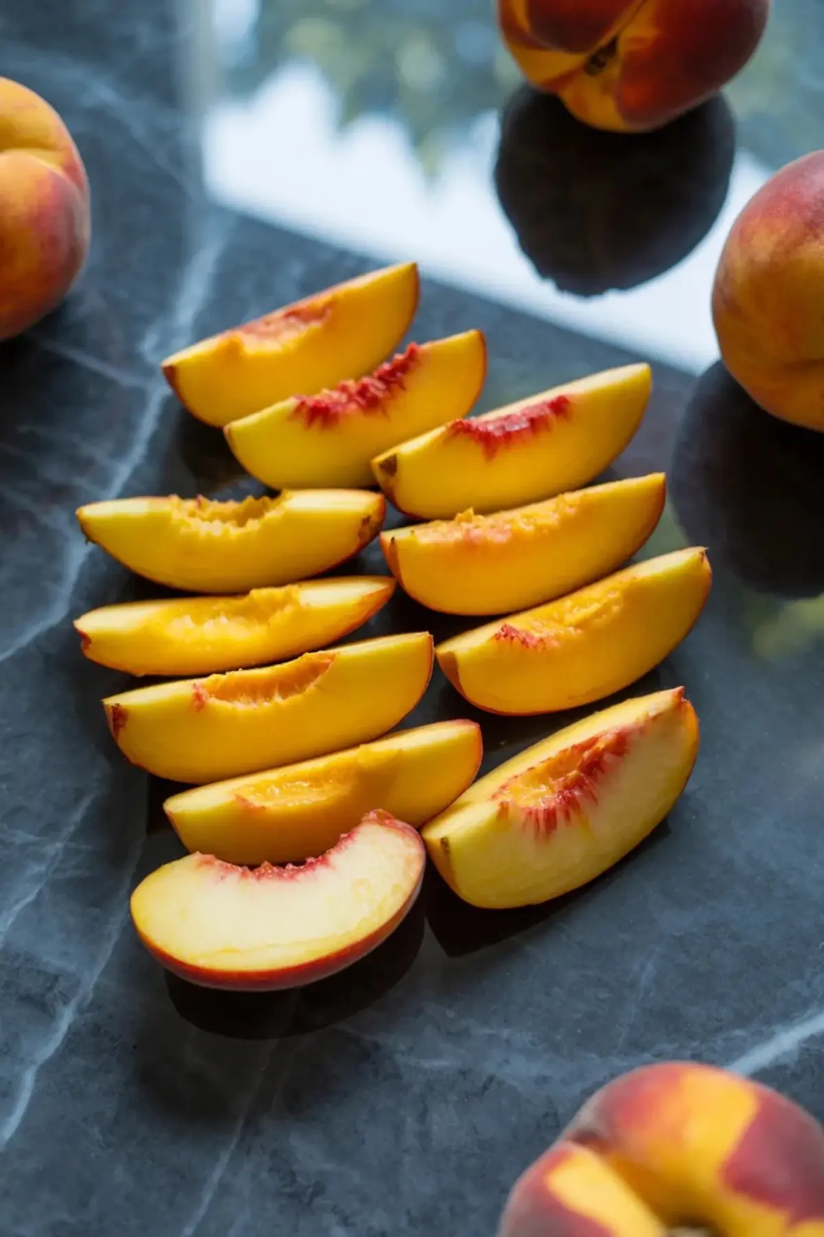 Fresh peach slices for peach yogurt bark are arranged on a dark marble surface.