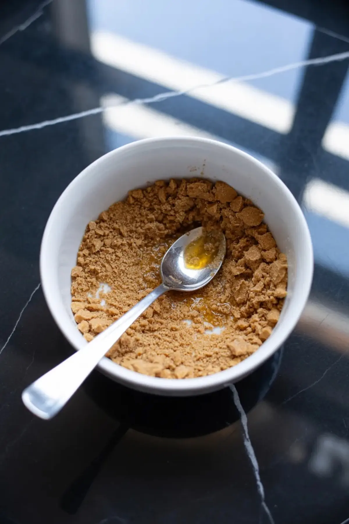 Graham cracker crumbs and melted butter are mixed in a bowl for the crust of strawberry swirl no-bake cheesecake bars.