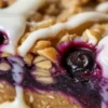 A plated blueberry oatmeal bar with thick lemon glaze shows the jammy blueberry filling, buttery oat topping, and sturdy crumb base.