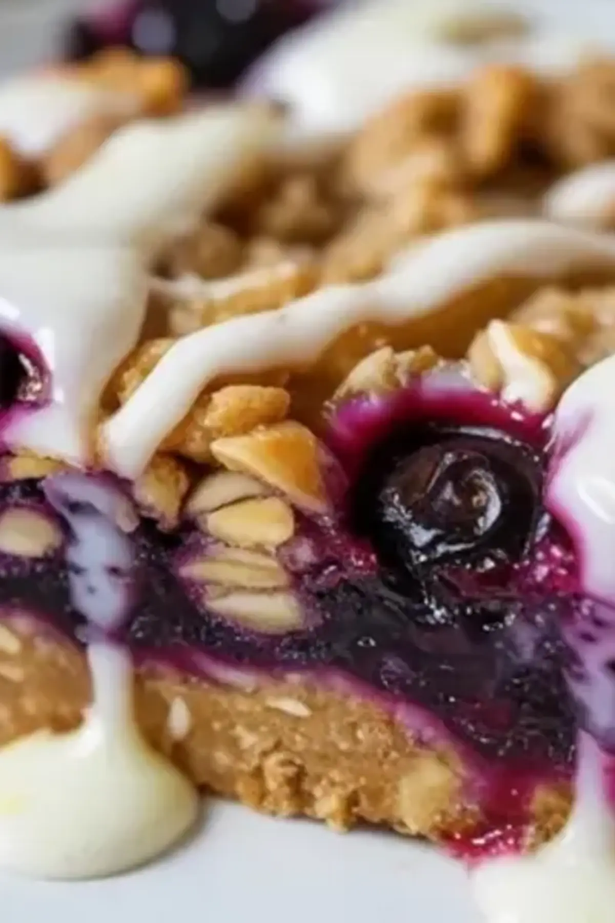 A plated blueberry oatmeal bar with thick lemon glaze shows the jammy blueberry filling, buttery oat topping, and sturdy crumb base.