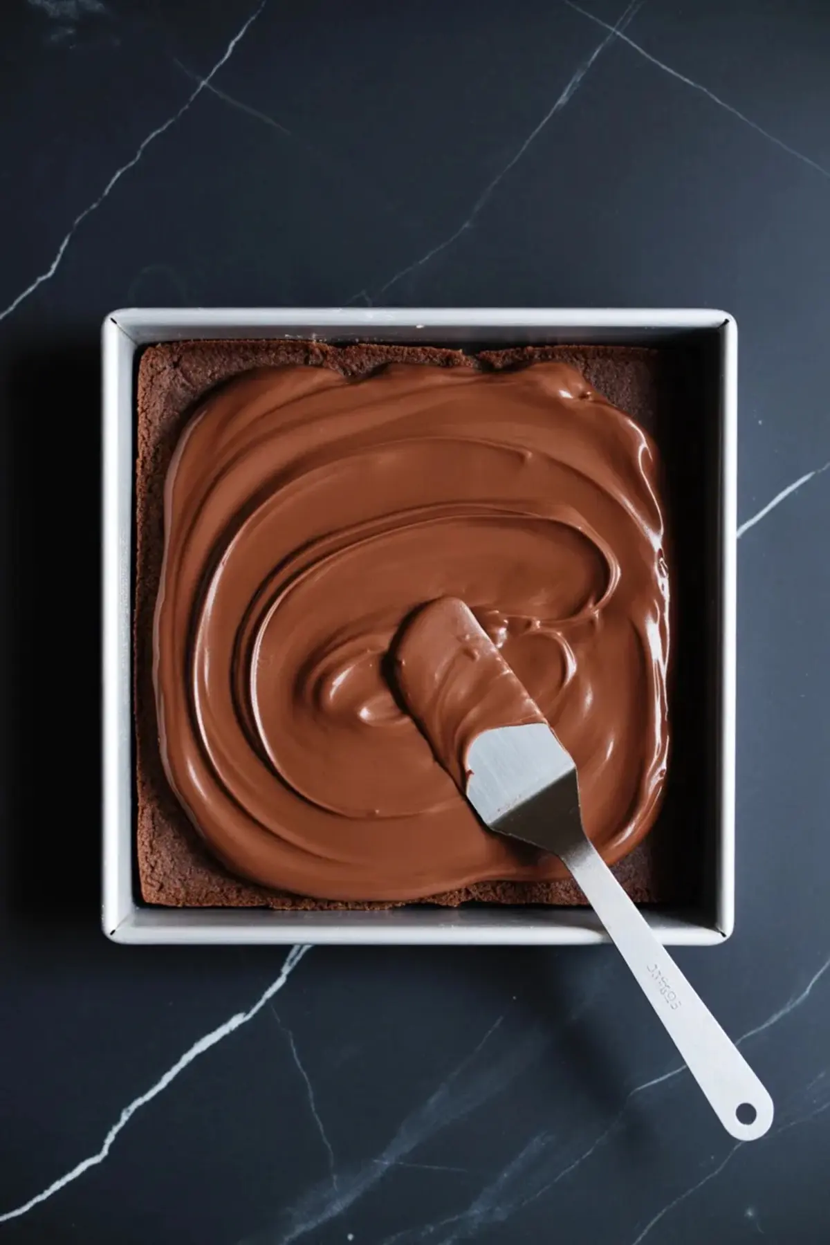 Chocolate cream pie filling is spread over a chocolate cookie crust in a square pan with an offset spatula.