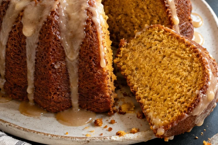 A glazed sweet potato pound cake on a speckled cream plate with one thick slice cut and tipped on its side, showing a moist golden-orange crumb under brown butter glaze drips, on a black stone counter.